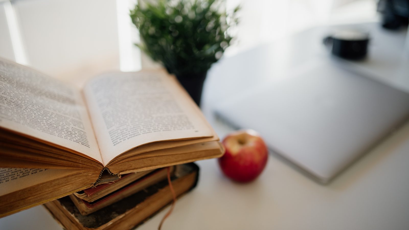 An open book next to a laptop and an apple on a study desk