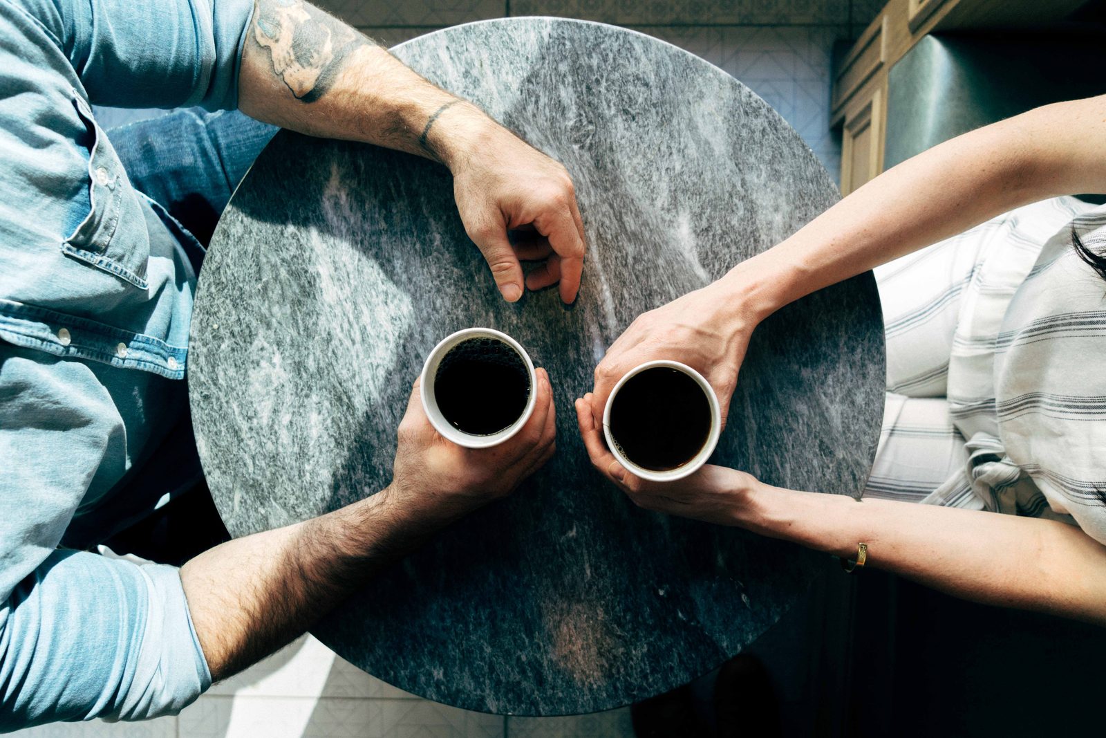 Two people talking over coffee, hands and cups on a table